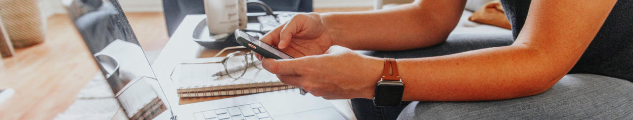 Image of a person's hands as they use a mobile phone and computer