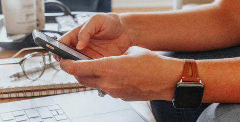 Image of a person's hands as they use a mobile phone and computer